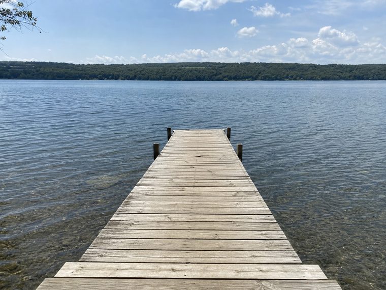 A wooden dock reaching into a calm lake under a summer sky